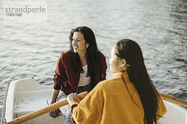 Lächelnde Frau sitzt mit einer Freundin im Ruderboot auf einem See