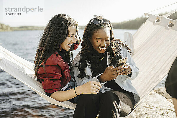 Glückliche Freundinnen benutzen ihr Smartphone  während sie in der Hängematte sitzen