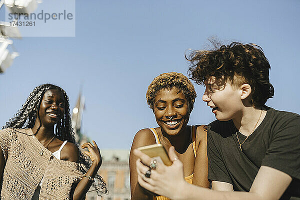 Teenager teilt sein Smartphone mit seinen Freunden an einem sonnigen Tag