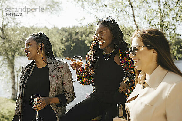 Glückliche Freundinnen trinken Wein am Seeufer