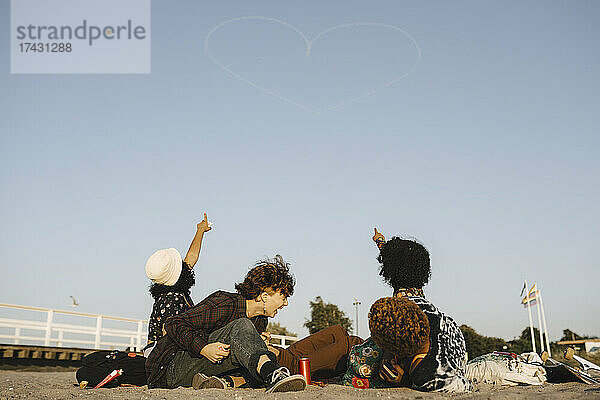 Teenager-Mädchen zeigen auf Herzform Dampffahne auf klaren Himmel während sonnigen Tag