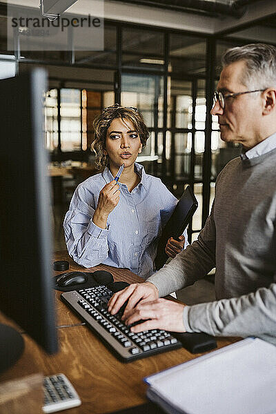 Weibliche Fachkraft diskutiert mit einem Geschäftsmann  der einen Computer am Schreibtisch benutzt