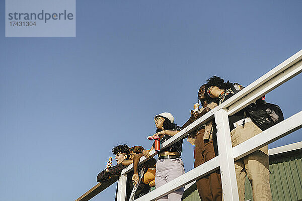 Low angle view of multiracial Freunde hängen am Pier gegen klaren Himmel