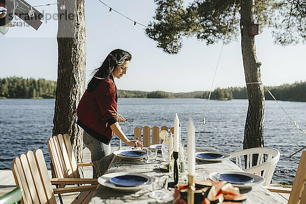 Junge Frau deckt den Tisch am See an einem sonnigen Tag