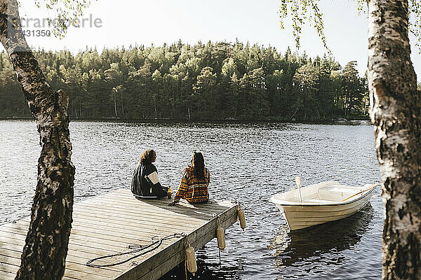 Freundinnen sitzen an einem sonnigen Tag auf einem Steg über dem See