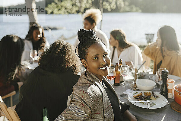 Porträt einer lächelnden Frau  die mit ihren Freundinnen auf einer Dinnerparty an einem sonnigen Tag sitzt