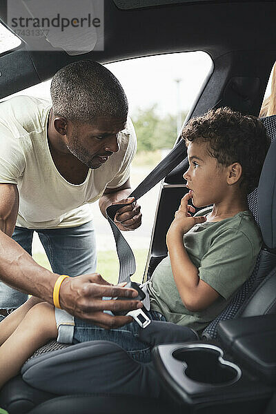 Vater im Gespräch mit seinem Sohn beim Anschnallen im Auto