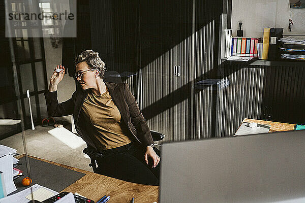 Unternehmerin wirft Papier  während sie am Schreibtisch sitzt