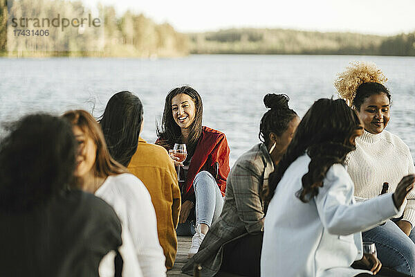 Lächelnde multirassische Freundinnen sitzen auf einem Steg am See