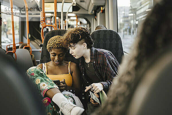 Jugendlicher schaut auf junge nicht-binäre Frau  die im Bus ein Smartphone benutzt