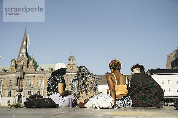 Oberflächenniveau Ansicht von multirassischen Freunden sitzen in der Stadt an einem sonnigen Tag