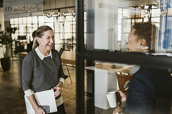 Reife Geschäftsfrau lacht mit männlichem Kollegen im Büro