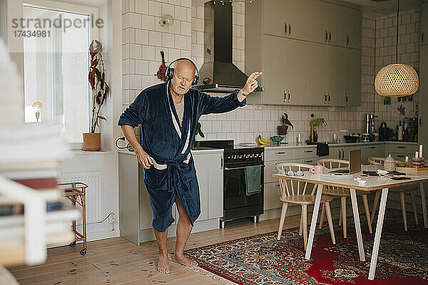 Älterer Mann tanzt  während er in der Küche über Kopfhörer Musik hört