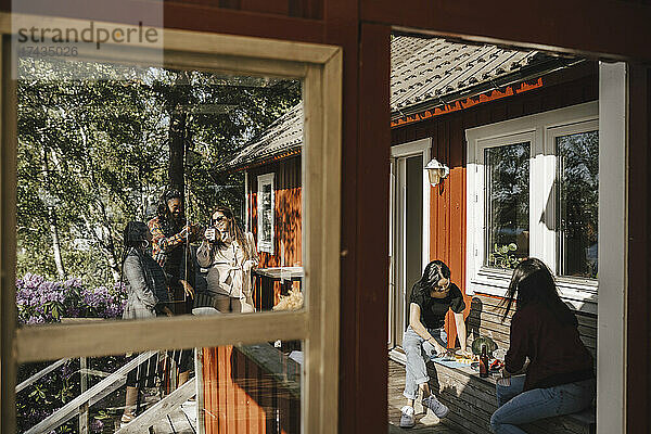 Weibliche Freunde beim Abendessen auf der Veranda vom Fenster aus gesehen