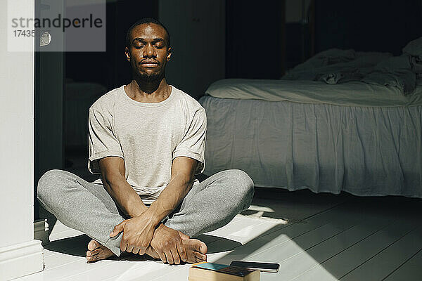 Mittlerer erwachsener Mann meditiert mit geschlossenen Augen im Sonnenlicht zu Hause