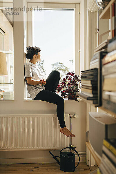 Junge Frau sitzt zu Hause am Fenster