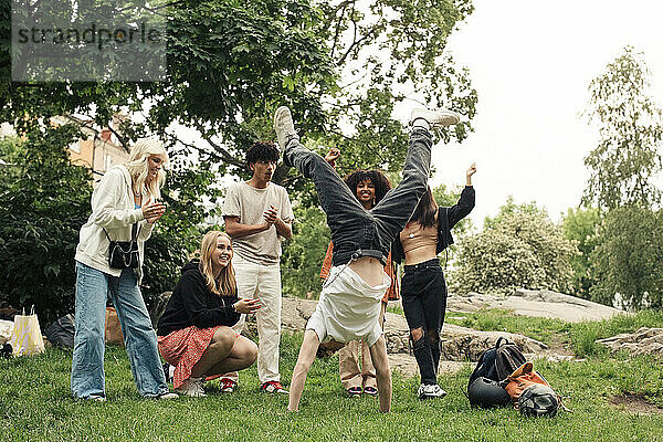 Multirassische Freunde jubeln einem Teenager zu  der im Park einen Handstand macht