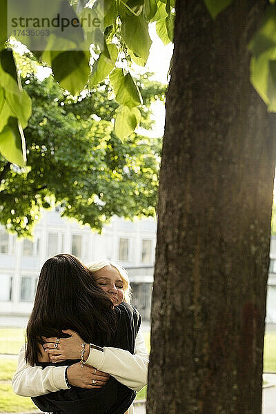 Freundinnen umarmen sich unter einem Baum im Park