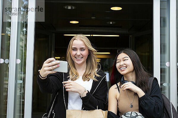 Lächelnde Freundinnen machen ein Selfie mit ihrem Smartphone im Einkaufszentrum