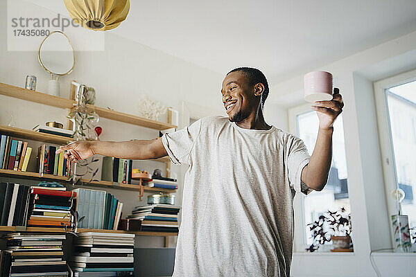 Glücklich Mitte erwachsenen Mann tanzen mit Kaffeetasse im Wohnzimmer zu Hause