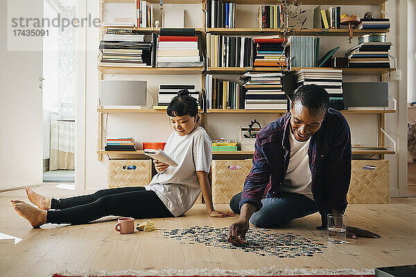Mann spielt Puzzle  während seine Freundin im Wohnzimmer ein Buch liest