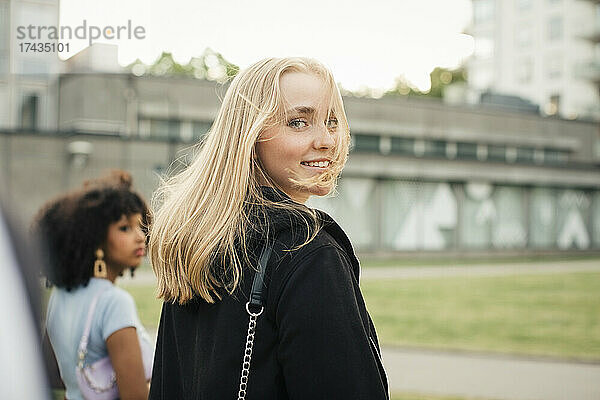 Lächelndes Teenager-Mädchen  das mit einer Freundin im Park spazieren geht