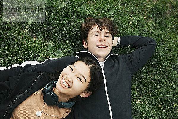 Lächelnde männliche und weibliche Freunde liegen im Gras