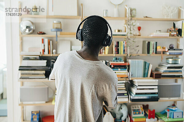 Rückansicht eines mittelgroßen erwachsenen Mannes  der zu Hause über Kopfhörer Musik hört