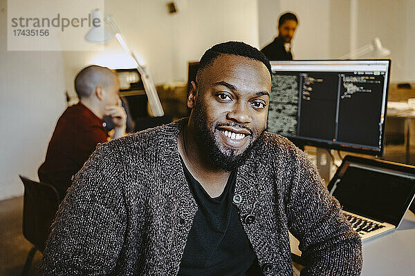 Porträt eines jungen männlichen Programmierers  der mit einem Kollegen am Schreibtisch in einem Start-up-Unternehmen arbeitet