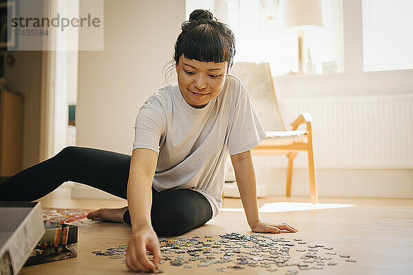 Lächelnde Frau beim Lösen eines Puzzles auf dem Boden im Wohnzimmer
