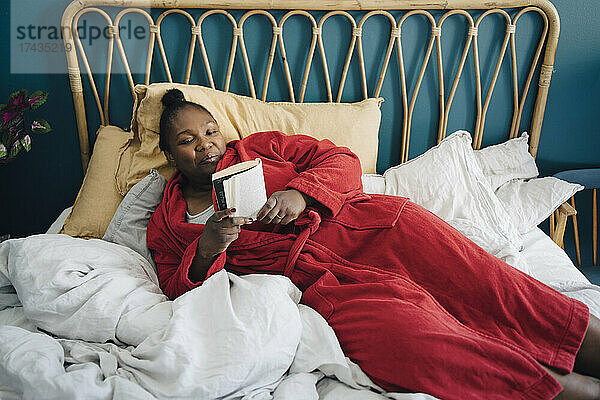 Mittlere erwachsene Frau liest ein Buch und entspannt sich auf dem Bett