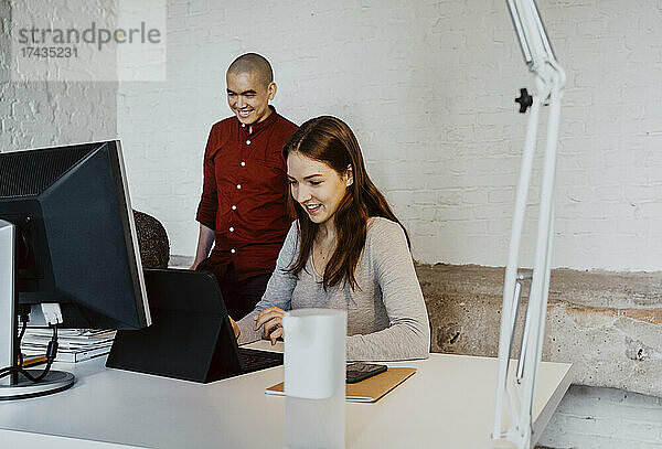 Lächelnder weiblicher Hacker mit Laptop bei der Arbeit mit Kollegen in einem Startup-Unternehmen