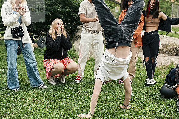 Männlicher Teenager macht Handstand mit Freunden im Park