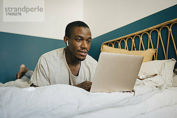 Mittlerer erwachsener Mann benutzt Laptop über dem Bett im Schlafzimmer