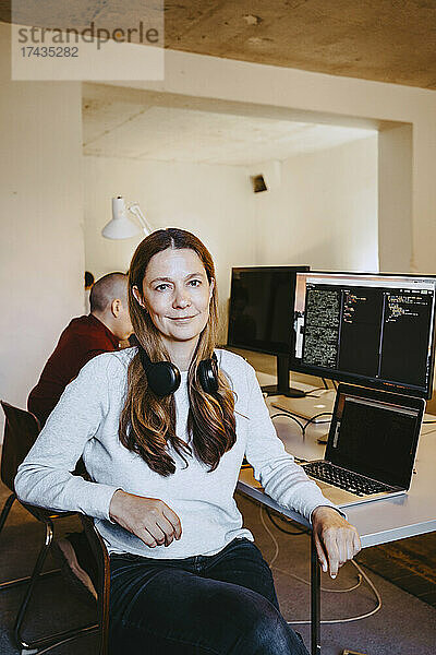 Porträt einer Programmiererin mit Laptop und Computer am Schreibtisch im Büro