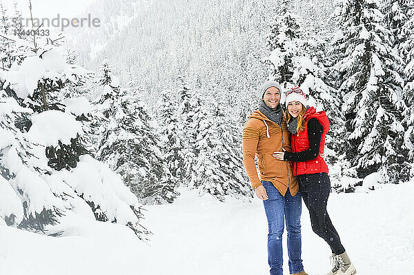 Lächelndes Paar  das im Winter zusammen auf Schnee steht