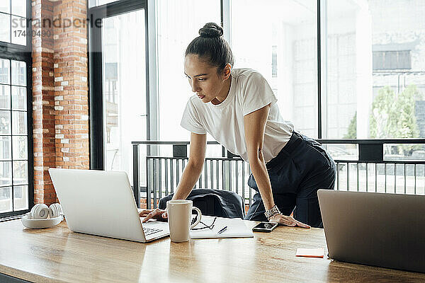 Weibliche Geschäftsfrau benutzt Laptop  während sie am Schreibtisch im Büro steht