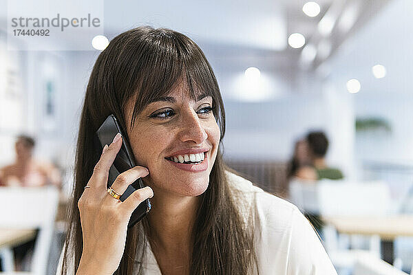 Glückliche Geschäftsfrau  die im Restaurant mit dem Smartphone spricht