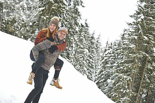 Mann gibt Frau im Winter Huckepackfahrt im Schnee