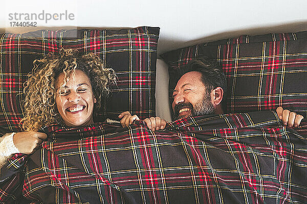 Glückliche Männer und Frauen lachen  während sie zu Hause im Bett liegen