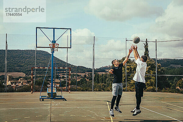 Junge Männer spielen an sonnigen Tagen Basketball auf dem Sportplatz