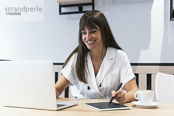 Weibliche Designfachfrau mit Laptop und Grafiktablett im Restaurant