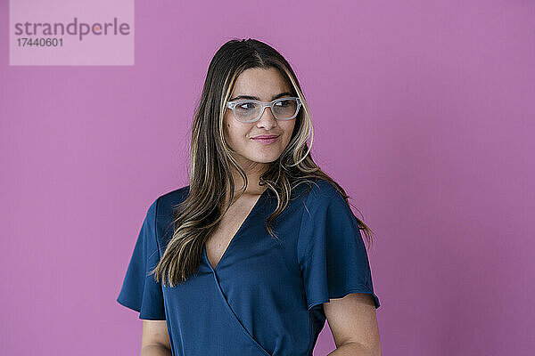 Lächelnde Geschäftsfrau mit Brille vor rosa Wand