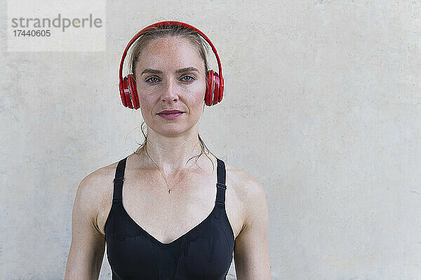 Sportlerin hört Musik über Kopfhörer vor der Wand