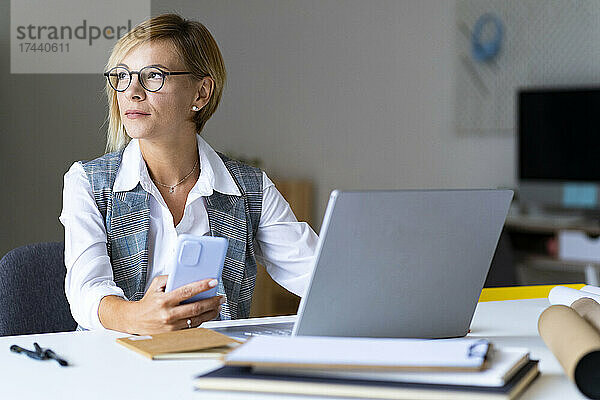 Geschäftsfrau mit Mobiltelefon sitzt am Schreibtisch im Büro
