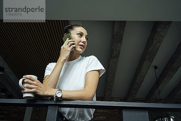 Berufstätige Frau  die im Büro mit dem Mobiltelefon spricht