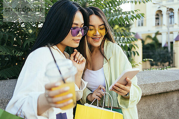 Lächelnde Freunde mit Sonnenbrille und Smartphone vor der Stützmauer