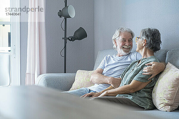 Lächelnder älterer Mann mit der Hand auf der Schulter  der die Frau im Wohnzimmer ansieht