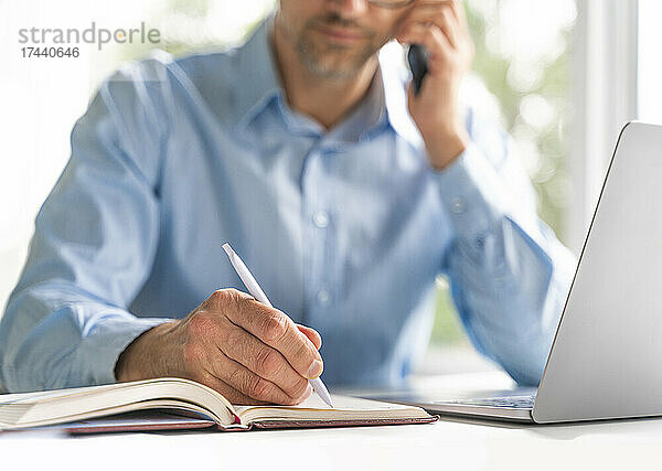 Reifer Geschäftsmann schreibt am Schreibtisch im Büro Tagebuch