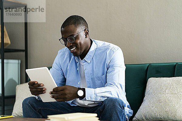 Lächelnder männlicher Freiberufler nutzt digitales Tablet  während er von zu Hause aus arbeitet